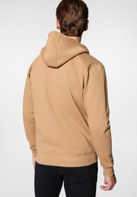 Brązowa bluza z kapturem o miękkim, teksturowanym wykończeniu, z prążkowanymi mankietami i dołem. Posiada kieszeń typu kangur i luźny krój.