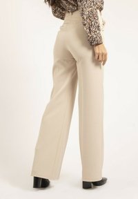 Pantalons larges beiges en tissu lisse, dotés d'une taille haute et de poches. Associés à un chemisier à motifs et des bottes à talons noires.