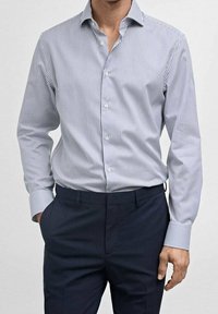 Raitapaita valkoisena ja laivastonsinisenä, pitkähihaisena, napitettava malli ja teräväkauluksena. Yhdistetty räätälöityjen laivastonsinisten housujen kanssa.