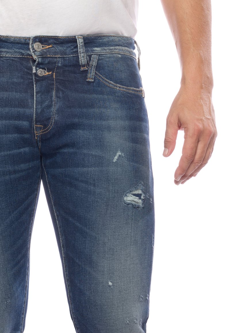 Jeans en denim bleu foncé avec accents déchirés, dotés d'une fermeture à bouton, d'un design à cinq poches et d'un léger dégradé sur les jambes.