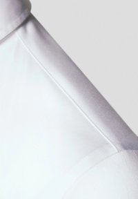 Biała satynowa tkanina ukazująca szew na ramieniu o gładkiej fakturze i subtelnym połysku. Czyste linie podkreślają dopasowane detale projektu.