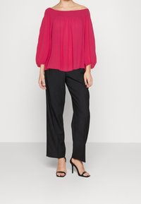 Blusa fucsia off-the-shoulder con scollo arricciato, maniche lunghe a palloncino, abbinata a pantaloni neri a gamba larga e tacchi neri con cinturini.