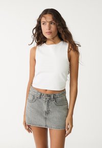 Vit ärmlös crop top i kombination med en höga midja, ljusgrå denim mini kjol med framfickor och knäppning.