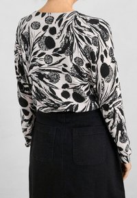 Sweter w czarno-białe kwiatowe wzory z długimi rękawami, okrągłym dekoltem i miękką fakturą, w połączeniu z czarną spódnicą dżinsową z tylnymi kieszeniami.