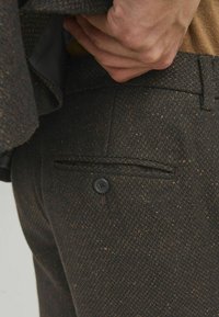 Bunde hlače od vune s smeškim ribljičastim uzorkom, elegantnom džepu i crnim dugmetom, s teksturiranom završnom obradom i prilagođenim krojem.