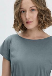 Kurzärmliges T-Shirt mit rundem Halsausschnitt in gedämpftem Türkis, aus weichem Material mit glatter Textur und lässiger Passform.
