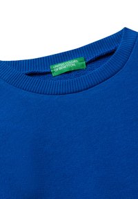 Maglione crewneck blu con colletto a coste e un'etichetta verde con la scritta "UNITED COLORS OF BENETTON" cucita all'interno del collo.