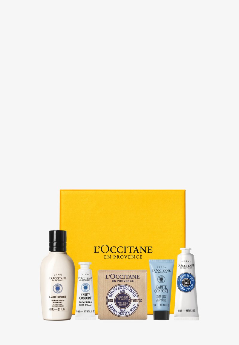 Cinq produits de soins L'Occitane en Provence comprenant une crème de douche, une crème pour les pieds, un savon au lait, une crème pour le corps et une crème pour les mains devant une boîte jaune.