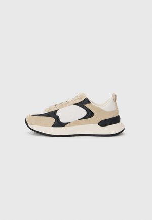 Sneaker beige e nera con materiali in suede e mesh, punta arrotondata, suola leggera e dettagli del logo prominenti sul lato.