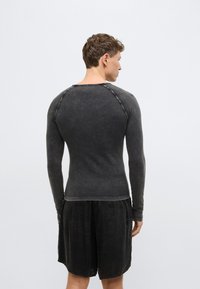Tričko s dlhými rukávmi v tmavošedej látke s mierne opotrebovanou textúrou, s kontrastným prešívaním a okrúhlym výstrihom.