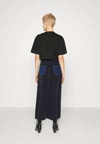 Zwarte crop T-shirt gecombineerd met een lange donkerdenim rok met blauwe patchzakken. Model draagt zwarte enkellaarsjes.