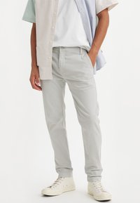 Man wearing light gray slim-fit pants, white sneakers, white T-shirt, and a multicolored vertically striped short-sleeve shirt.