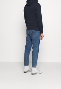 Marinblå hoodie med en känguruficka, kombinerad med ljusblå avsmalnande jeans. Vita sportskor. Enkel design, inga synliga mönster.