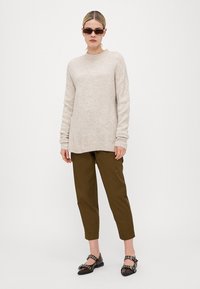Beige oversized genser laget av et mykt materiale med ribbet mansjetter og kant, kombinert med olivengrønne avsluttede bukser og svarte sko.