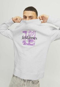 Grå sweatshirt med høj hals, der har et lilla blomsterdesign på ryggen og sort "Jack & Jones" logo. Fremstillet af bomuldsmateriale, afslappet design.