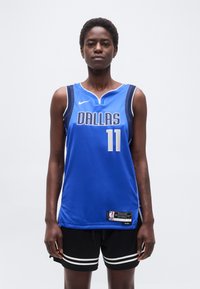 Άτομο που φοράει μπλε φανέλα μπάσκετ Dallas με αριθμό 11 και μαύρο σορτς με λευκές ρίγες, στέκεται μπροστά σε απλό λευκό φόντο.