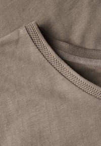 Tessuto di cotone marrone con una texture liscia, caratterizzato da un collo rotondo e dettagli in contrasto lungo il colletto.