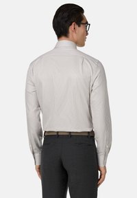 Pruhovaná košile s dlouhým rukávem a klasickým límcem; materiál je jemný a lehký. Kombinováno s tmavými kalhotami a opaskem s potiskem puntíků.