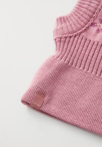 Zbliżenie na złożony różowy sweter dzianinowy z prążkowaną fakturą oraz małą metką z napisem "mixo" na białym tle.