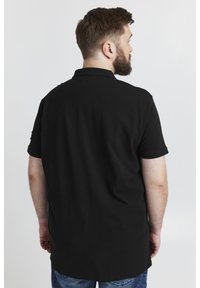 Must must värvitud polo särk, mis on valmistatud puuvillast, klassikalise krae ja lühikeste varrukatega. Seljal on kerge kumer serv ja minimaalne kaunistus.
