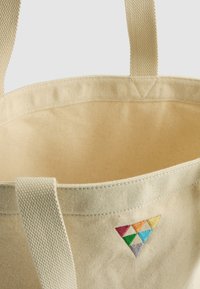 Sac en toile de couleur écrue avec une finition texturée. Présente un motif triangulaire brodé coloré d'un côté et des anses en tissu solides.