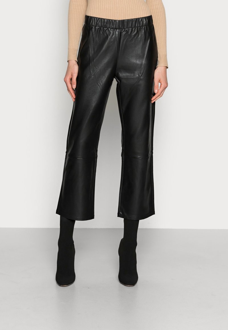 Culottes en cuir noir avec une taille élastique, présentant une texture lisse et une longueur raccourcie, associées à des bottines noires ajustées.