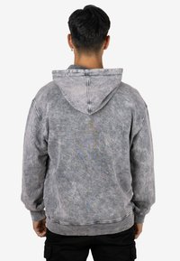 Sudadera con capucha gris de apariencia texturizada, con capucha ajustable mediante cordones y puños acanalados. El material parece suave y informal.