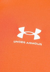 Oranžno sintetično blago z gladko teksturo, ki ima belo Under Armour logo nameščen na sredini.