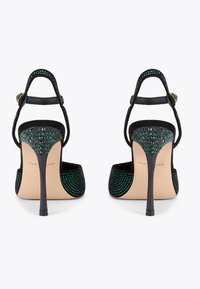 Czarne sandały na wysokim obcasie z zielonymi ozdobami z kamieni i zamszowym wykończeniem. Posiadają smukły obcas i pasek na kostce. Logo marki na wewnętrznej podeszwie.