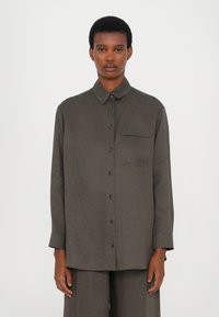 Camicia marrone con bottoni in tessuto leggero, con colletto, maniche lunghe, taschino frontale e una leggera texture. Progettata per un fit rilassato.