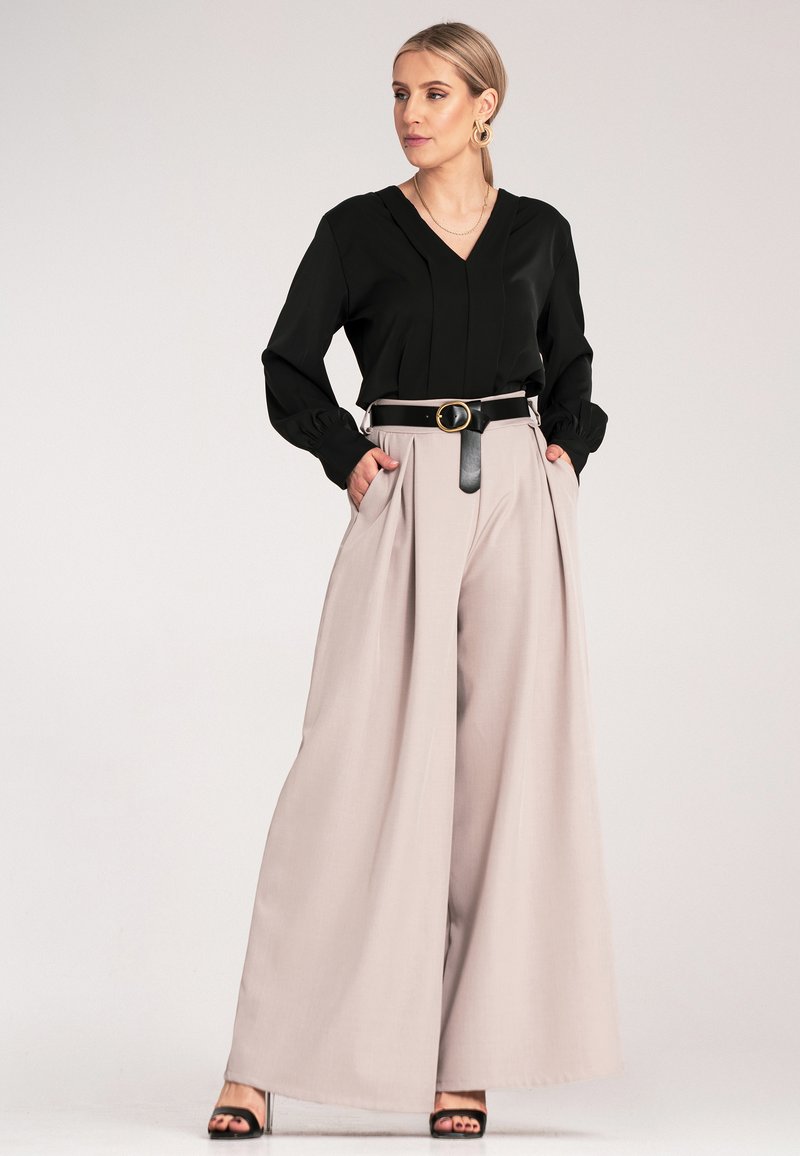 Czarna blouse w serek z długimi rękawami, zestawiona z beżowymi spodniami o wysokim stanie i szerokich nogawkach. Uzupełniona czarnym paskiem i szpilkami.
