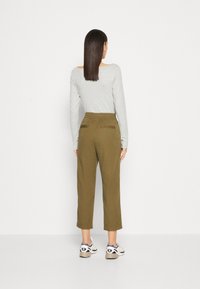 Chemise grise à manches longues, pantalon tapered vert olive avec une taille élastique, comportant deux poches arrière, associé à des baskets blanches et grises.