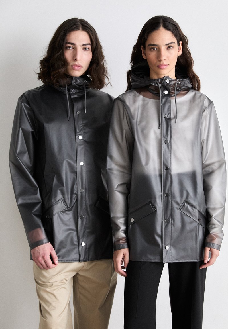 Veste de pluie noires et grises translucides avec capuchons ajustables, fermetures à bouton-pression et poches avant. Matière lisse et résistante à l'eau.