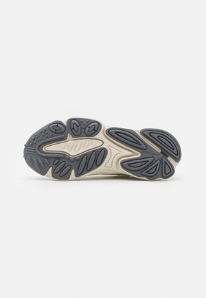 Semelle de chaussure avec bande de roulement en caoutchouc noir et beige présentant des formes ovales et courbes pour l'adhérence et la flexibilité, sur un fond blanc uni.