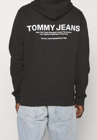 Felpa nera in cotone, con grande testo bianco sul retro. Polsini e orlo a coste. Abbinata a jeans in denim blu chiaro.