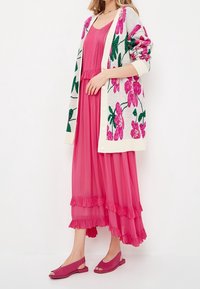 Roze bloemen cardigan over een geplooide roze maxi-jurk met ruches, aangevuld met open teen magenta schoenen. Getextureerde brei en gladde stof.