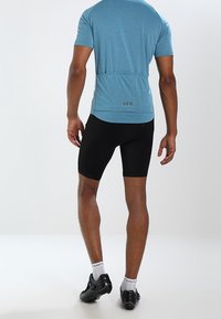Světlomodré sportovní tričko s krátkými rukávy a černé cyklistické šortky; mají štíhlý střih, hladkou tkaninu a logo na zádech.