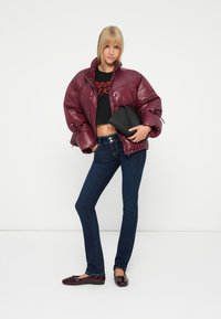 Burgunderfarget puffjakke med blank finish, svart cropped t-skjorte, mørkeblå jeans og svart håndveske; modell iført burgunder loafers.