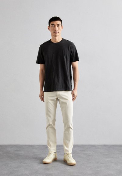 Black short-sleeve t-shirt, cream slim-fit pants, and light sneakers. Simple, relaxed fit with a solid color scheme. Smooth fabric texture.