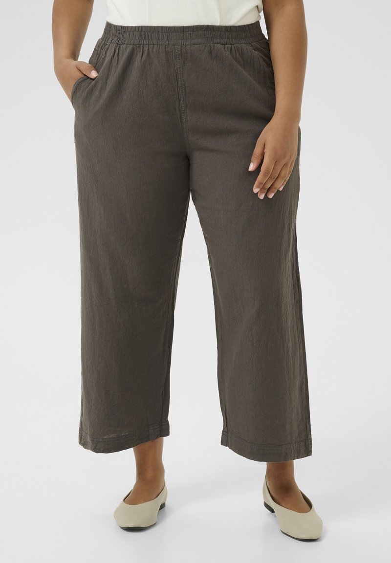 Pantalons larges gris avec une taille élastique et des poches latérales, en tissu léger avec une finition texturée. Les chaussures sont d'un beige clair.