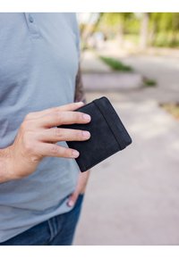 Black leather wallet with a smooth texture, featuring a card slot on one side and minimalistic design, held in a hand outdoors.