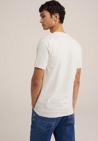 Baltas kokvilnas T-krekls ar īsām piedurknēm, apaļu kakla izgriezumu un brīvu piegriezumu, kombinēts ar ziliem džinsiem ar dzelteniem izšuvuma akcentiem.