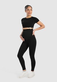 Top deportivo corto negro y leggings de cintura alta, ambos en tela elástica, combinados con zapatillas blancas. Presenta un diseño de soporte para mayor comodidad.