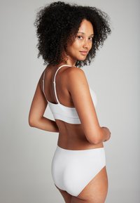 Reggiseno bianco senza cuciture e mutandine a vita alta coordinate, con sottili spalline regolabili e tessuto morbido, viste da dietro.