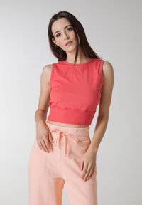 Koralfarvet, ærmeløs crop top med ribbet kant, parret med ferskenfarvede, højdenede bukser med snørelukning i taljen.