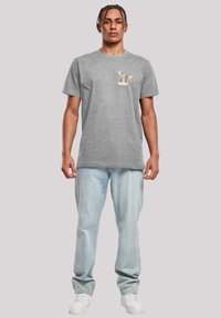 Grå bomull T-skjorte med korte ermer, med et cartoon hundedesign på brystet. Sammen med lyseblå denimjeans og hvite joggesko.