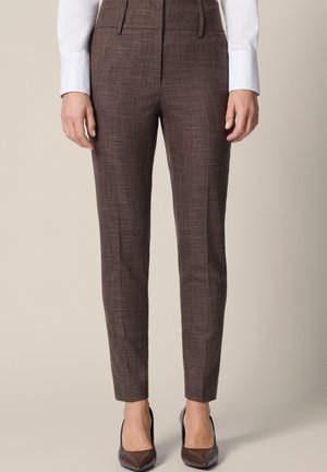 Brązowe, dopasowane spodnie w stylu slim-fit noszone z białą koszulą z długim rękawem i brązowymi szpiczastymi szpilkami, pokazane od talii do stóp.