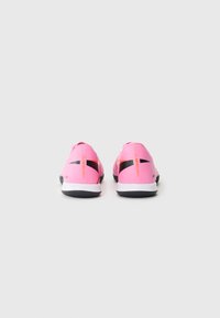 Chaussures de sport roses avec accents noirs, présentant un design épuré, un matériau texturé et une semelle blanche contrastante. Support de talon robuste inclus.