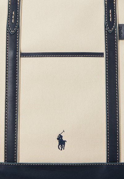 Kanvasový batoh v krémovej farbe s námorníckymi koženými akcentmi, s detailným prešívaním a malým námorníckym vyšitým logom jazdca na koni.
