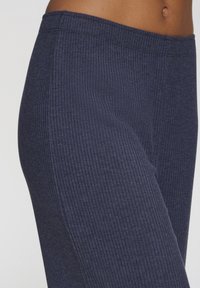 Mornarske rebraste legging hlače z mehkimi tkaninami in elastičnim pasom, ki prikazujejo vertikalne črte in prilegajoč dizajn brez žepov.